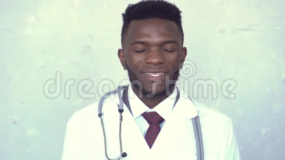 前景特写一位非洲男医生他穿着白色的实验室外套和听诊器站在混凝土墙上视频的预览图