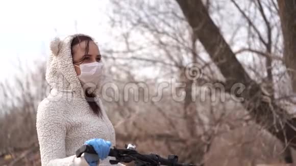 戴着医用口罩和手套的年轻女子骑着自行车站在农村手握舵保护妇女视频的预览图