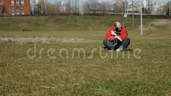 一个男人坐在草地上抱着他的德国牧羊犬在草地上慢动作视频的预览图