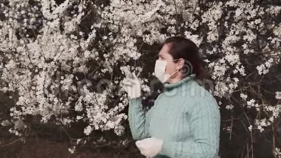 戴着医用面具的年轻女子欣赏一棵开花的树视频的预览图
