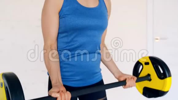 穿运动服的强壮漂亮的女孩用杠铃做二头肌运动她在家里的客厅里接受训练视频的预览图