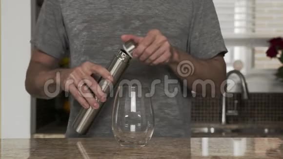 穿着灰色T恤的年轻人在一个漂亮时尚的厨房里用热水瓶或塑料瓶把水倒入玻璃杯中视频的预览图