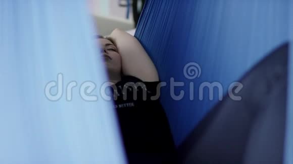 年轻性感的女人躺在蓝色的吊床上闭着眼睛瑜伽课后放松视频的预览图