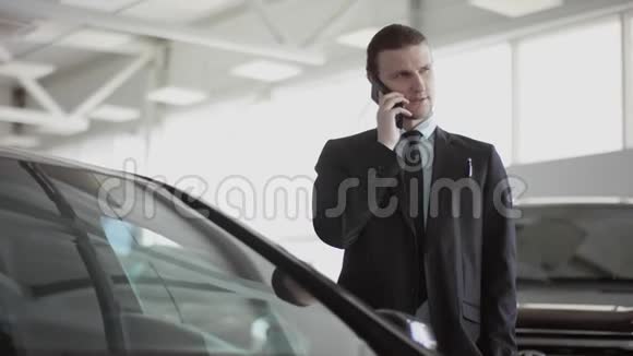 年轻人在打电话站在汽车沙龙里男人在打电话交流微笑他正在选车视频的预览图
