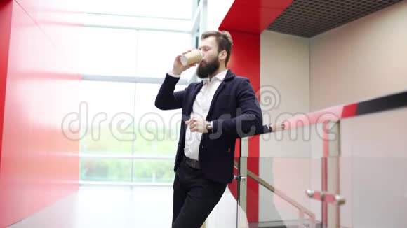 在现代办公大楼里一个思想的人靠在篱笆上喝着咖啡从前面看严重视频的预览图
