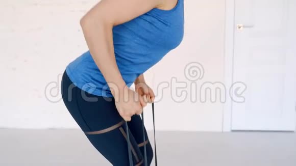 穿运动服的强壮漂亮的女孩用橡胶扩张器在背部肌肉上做运动她正在接受培训视频的预览图