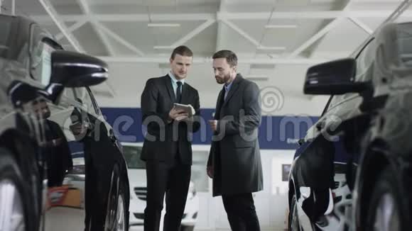 汽车经销商经理用平板电脑介绍新车站在汽车经销店的顾客正在倾听视频的预览图