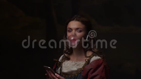 中世纪的少女穿着老式服装的少女使用智能手机吹泡泡糖视频的预览图