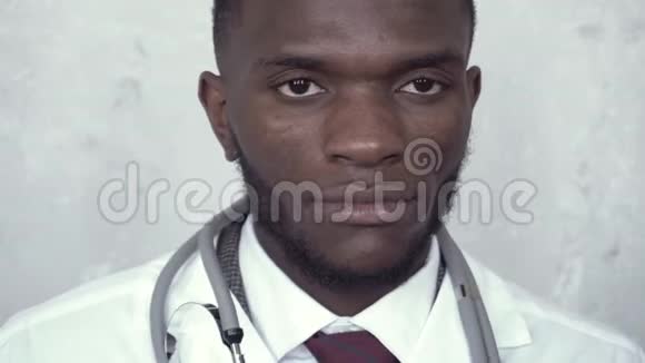 特写一位非洲男医生的肖像他穿着一件白色的实验室外套站在混凝土墙上取出一个听诊器视频的预览图
