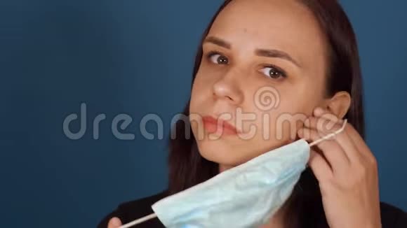 一幅年轻女子戴着医疗面具的肖像在蓝色背景下被隔离在家里成年女性视频的预览图