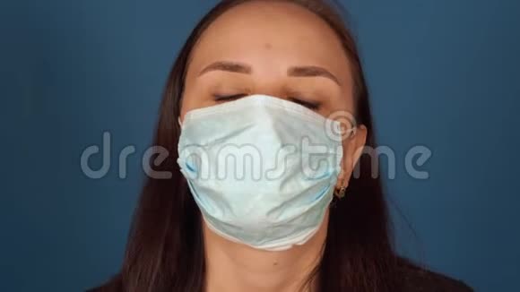年轻女性从脸上摘下医疗面具的肖像在蓝色背景下被隔离在家里成年女性视频的预览图