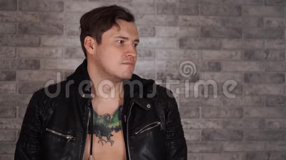 一位身穿黑色夹克胸前有纹身的英俊男子在灰色砖墙上摆出姿势视频的预览图