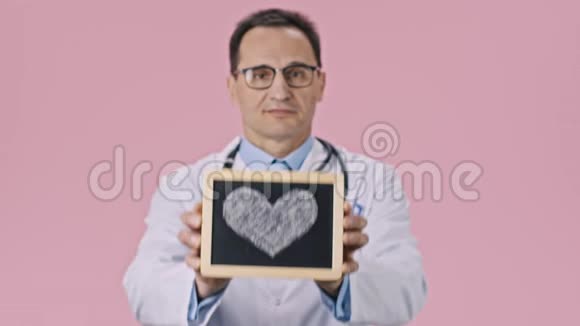 微笑男医生用粉红色背景的粉笔心显示药片视频的预览图