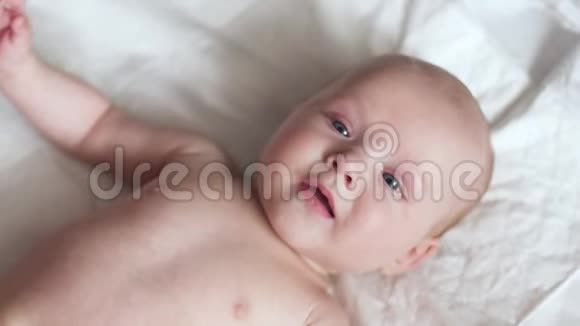 快乐的新生婴儿躺在床上尿布上移动双手微笑着试图交谈视频的预览图