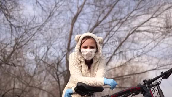 戴着医用口罩和手套的年轻女子站着在乡下骑自行车女性保护自己视频的预览图