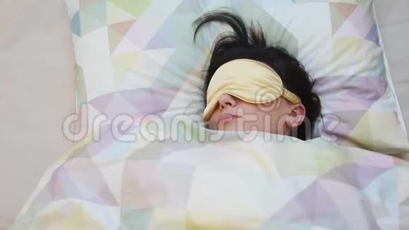 俯视清晨醒来的年轻女子戴着睡眠面具睡后伸展身体一个睡女人视频的预览图