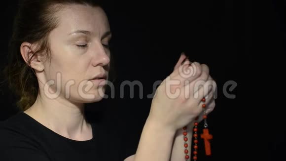 年轻女子在黑暗中用十字架祈祷念珠视频的预览图