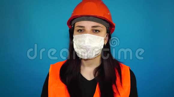 女建筑工人穿着工作服在蓝色背景上从脸上摘下医疗面罩视频的预览图