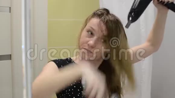 一位年轻女子在镜子前的浴室里用吹风机擦干头发视频的预览图
