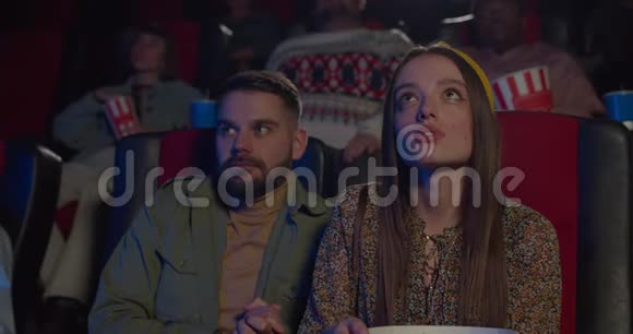 大胡子男抱着坐在他旁边的漂亮女孩在电影院年轻女孩在电影院约会时看上去很开心视频的预览图
