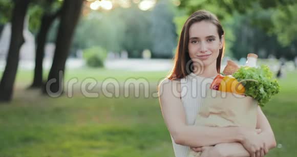 一幅迷人的女人微笑着拿着带食物的纸袋对着镜头的肖像站着摆姿势的漂亮女孩视频的预览图