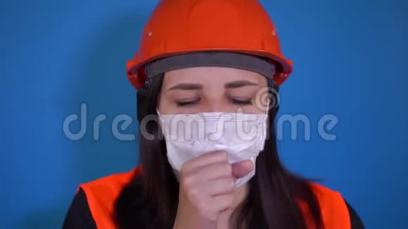 女建筑工人穿着工作服戴着医用口罩蓝底咳嗽感染威胁的概念视频的预览图
