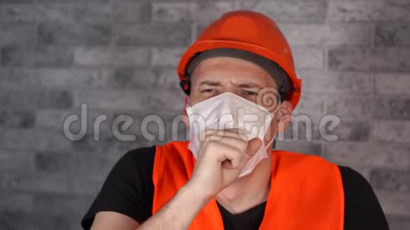 男施工工着工作服和医用口罩在灰砖墙脸背景上咳嗽威胁概念视频的预览图