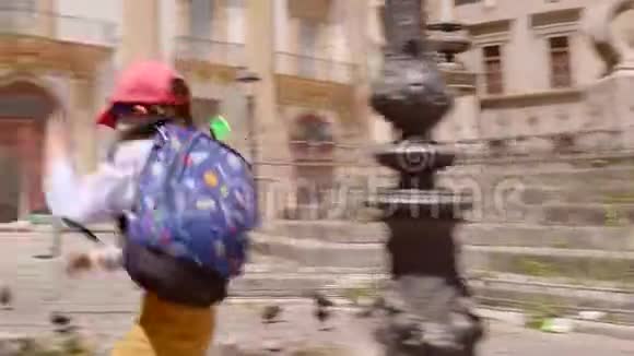 穿着时髦衣服的可爱男孩在巴勒莫广场上奔跑追逐鸽子视频的预览图