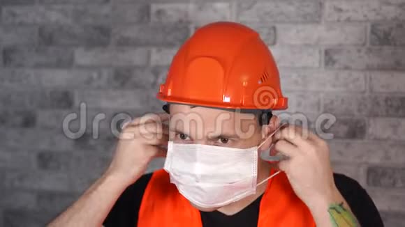 穿工作服的男建筑工人在灰砖墙上戴医用口罩视频的预览图
