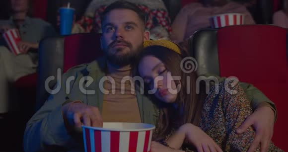 电影中睡在男朋友肩膀上的漂亮女孩的正面景色吃爆米花和拥抱的大胡子视频的预览图