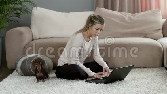 金发女孩坐在笔记本电脑上狗狗在家地毯上视频的预览图
