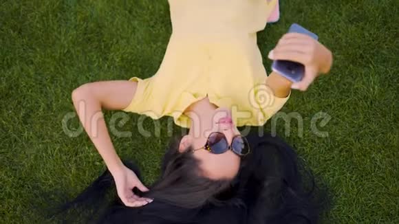 开心地笑着拉蒂诺黑发女孩躺在草地上自拍4K视频的预览图