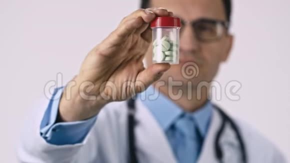中年男性医生出示透明罐子上面有绿色药丸白色背景视频的预览图