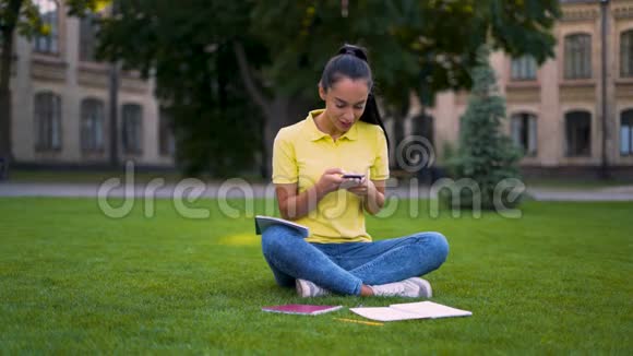 聪明的女学生坐在公园的草地上在手机上拨打短信4克视频的预览图