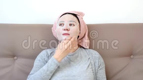 年轻女子在家里脸上戴着日本或韩国的化妆面具躺在沙发上女子美容常规视频的预览图