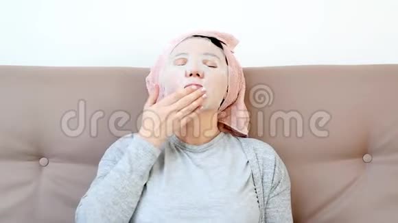 年轻女子在家里脸上戴着日本或科里安的化妆面具躺在沙发上女子美容常规视频的预览图