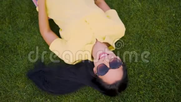 戴太阳镜的快乐开朗的女孩躺在草地上享受生活4K视频的预览图