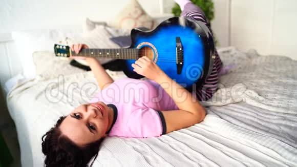 年轻女子在卧室弹吉他年轻女子在床上弹吉他她喜欢业余时间美丽美丽视频的预览图