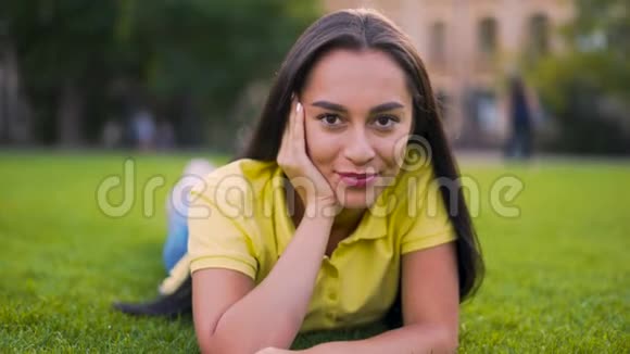 特写肖像一个友好的女孩躺在草地上看着相机4K视频的预览图