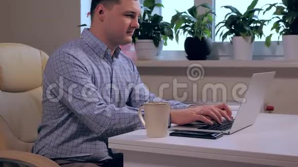 坐在现代办公桌前用笔记本电脑打字的男人视频的预览图