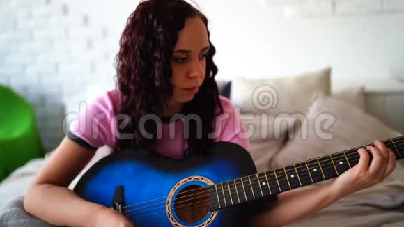 年轻女子在卧室弹吉他年轻女子在床上弹吉他她喜欢业余时间美丽美丽视频的预览图