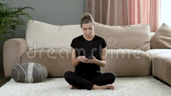 穿黑色衣服的女孩在家坐在沙发旁边的地毯上打视频电话视频的预览图