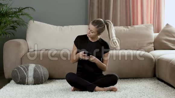 穿黑色衣服的女孩在地毯沙发上回家在电话上留言视频的预览图