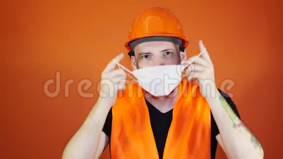 男建筑工人穿着工作服在橙色背景下从脸上摘下医用口罩视频的预览图