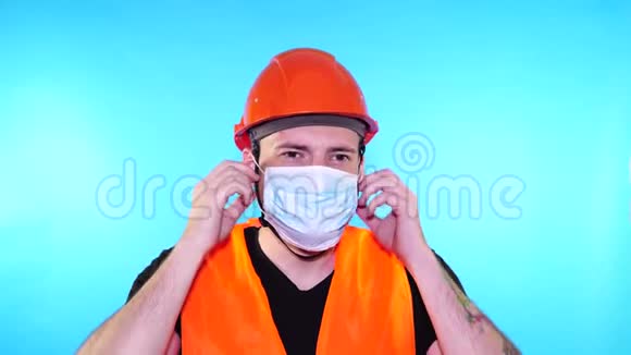 男建筑工人穿着工作服在蓝色背景上从脸上摘下医疗面罩视频的预览图