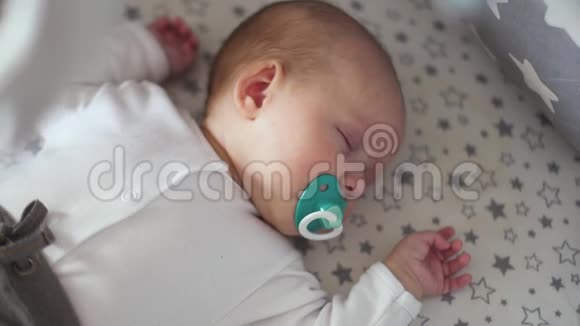 一个刚出生的婴儿睡在婴儿床上嘴里放着蓝色的奶嘴视频的预览图