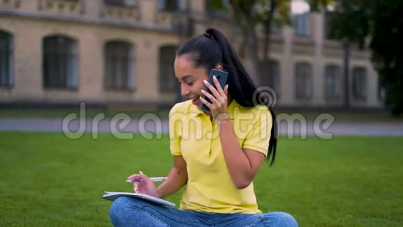 漂亮的拉丁女孩坐在公园里打电话那个女孩正在做作业4K视频的预览图