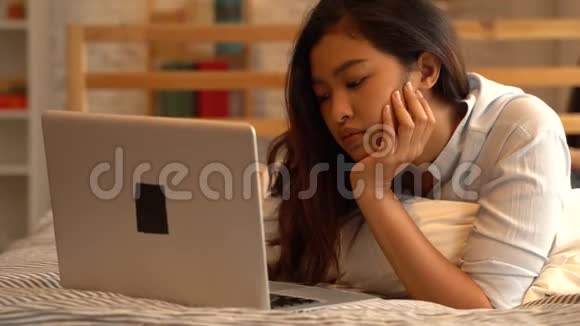 无聊的年轻亚洲女孩躺在床上在家里卧室工作女性自由职业者视频的预览图