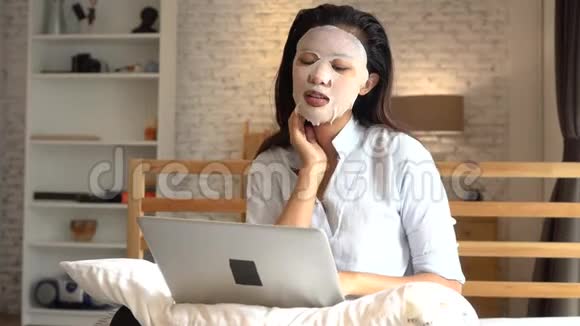 年轻的亚洲女孩在卧室里忙着用电脑笔记本电脑时脸上戴着面膜的肖像女人视频的预览图