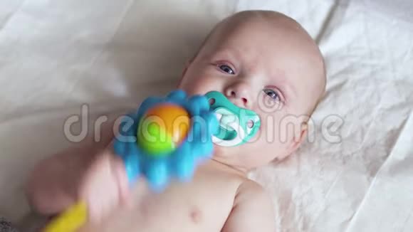 幼儿手里拿着玩具躺在尿布上试着咬它视频的预览图